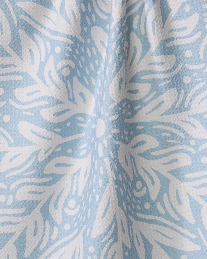The Outwards kitchen towel by Graphics and Grain, in light blue recycled fabric, features a white intricate floral and leaf pattern with a subtly textured surface and gentle vertical folds.