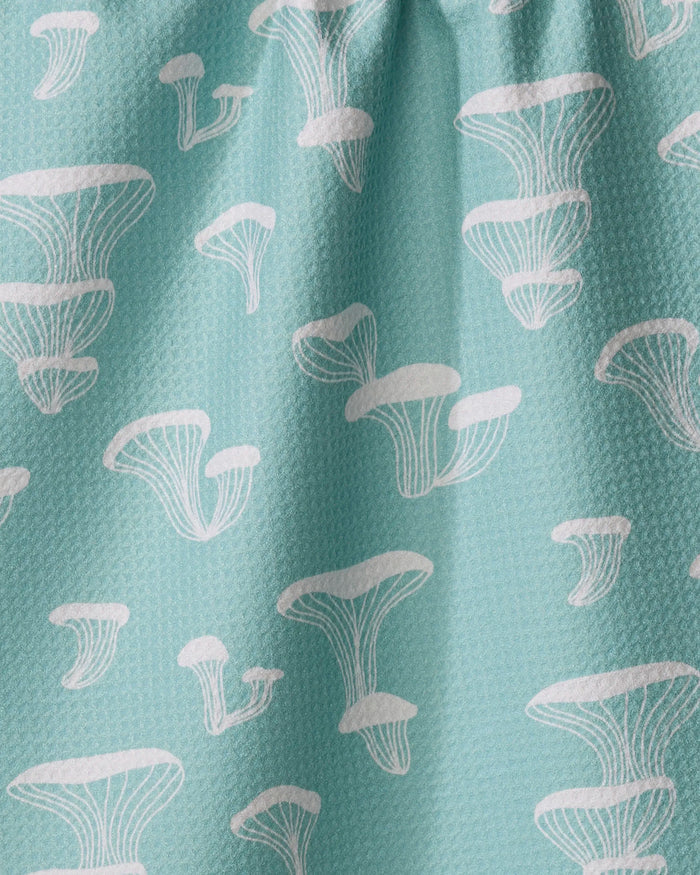 The Amberleigh Adoff Oyster Shroom is a light blue textured kitchen tea towel featuring a white stylized mushroom pattern. Made from recycled materials, this ultra-absorbent towel brightens up any kitchen.