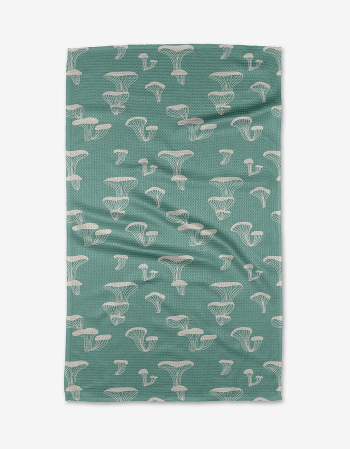 The Oyster Shroom tea towel by Amberleigh Adoff features white outlined mushrooms on green, is made from recycled materials, has mild wrinkles, and is shown flat on a white background.