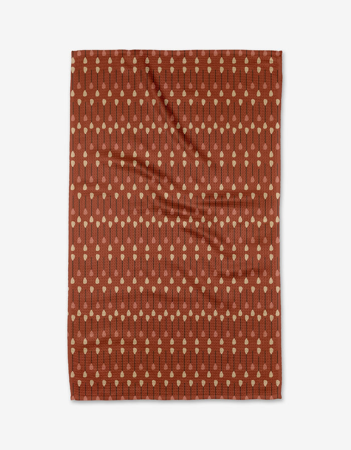 The Coit Creative Paddles and Oars tea towel is rust-colored, rectangular, and made from recycled materials, featuring beige dotted lines in a paddle-inspired pattern, shown flat on a white background.