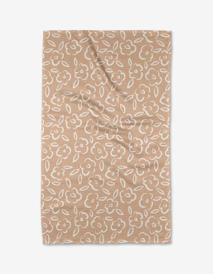The Painted Bloom kitchen towel by Hufton Studio features a tan color with a white floral and leaf pattern all over. Displayed flat on a white background, the towel shows some light folds and is crafted from recycled materials.