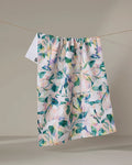 The "Painted Foliage" tea towel by Rachel Parker, crafted from recycled materials and featuring a leafy floral design, hangs on a clothesline against a neutral background.