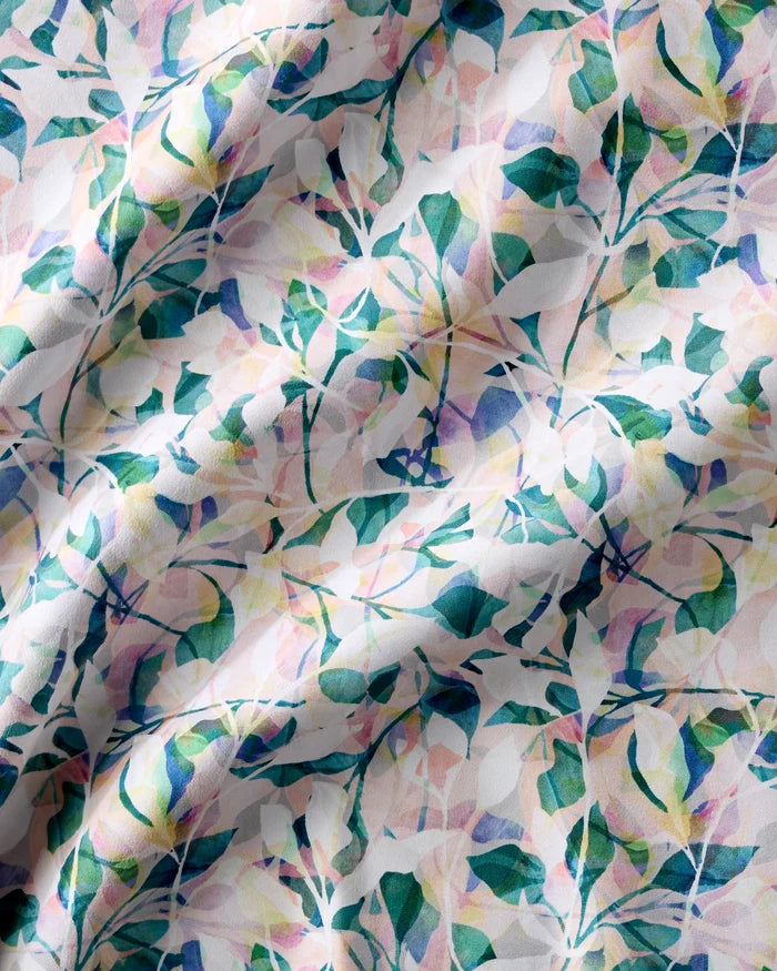 A close-up of crumpled Painted Foliage cloth napkins by Rachel Parker, showing a colorful abstract floral pattern in pastel green, pink, and blue on white. Light and shadow emphasize the folds and texture of this recycled dinner napkin set.