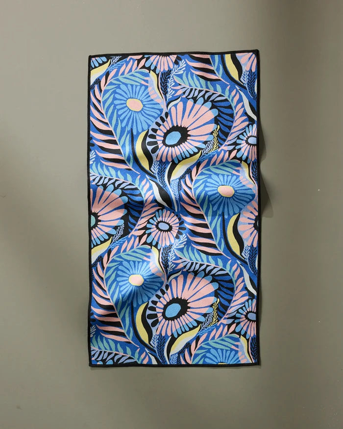 Palm Beach" by Masha Volnova is a rectangular scarf with bold blue, pink, yellow, and black floral designs. Ultra-absorbent and quick-drying, it doubles as a stylish fitness towel. Displayed on a beige background.