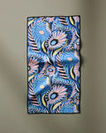 Palm Beach" by Masha Volnova is a rectangular scarf with bold blue, pink, yellow, and black floral designs. Ultra-absorbent and quick-drying, it doubles as a stylish fitness towel. Displayed on a beige background.