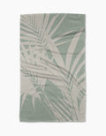The Palm Breeze blanket by Geometry features a light green and beige palm leaf pattern on durable Geoweave fabric, creating a tropical, modern look. Shown laid flat on a white background.
