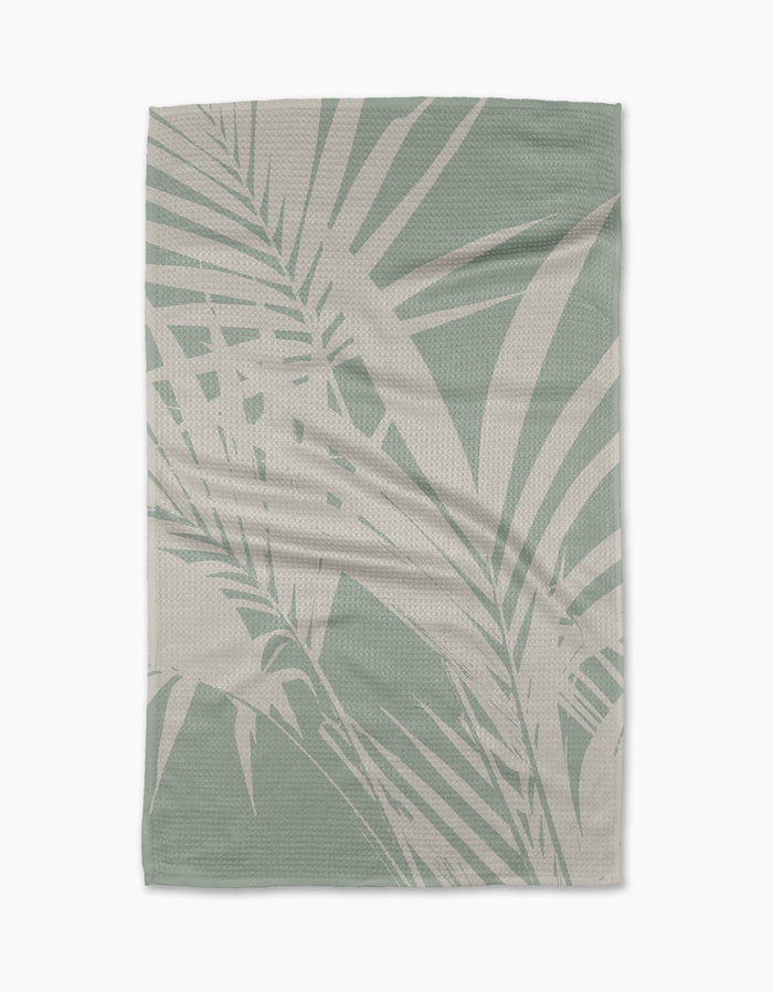 The Palm Breeze blanket by Geometry features a light green and beige palm leaf pattern on durable Geoweave fabric, creating a tropical, modern look. Shown laid flat on a white background.