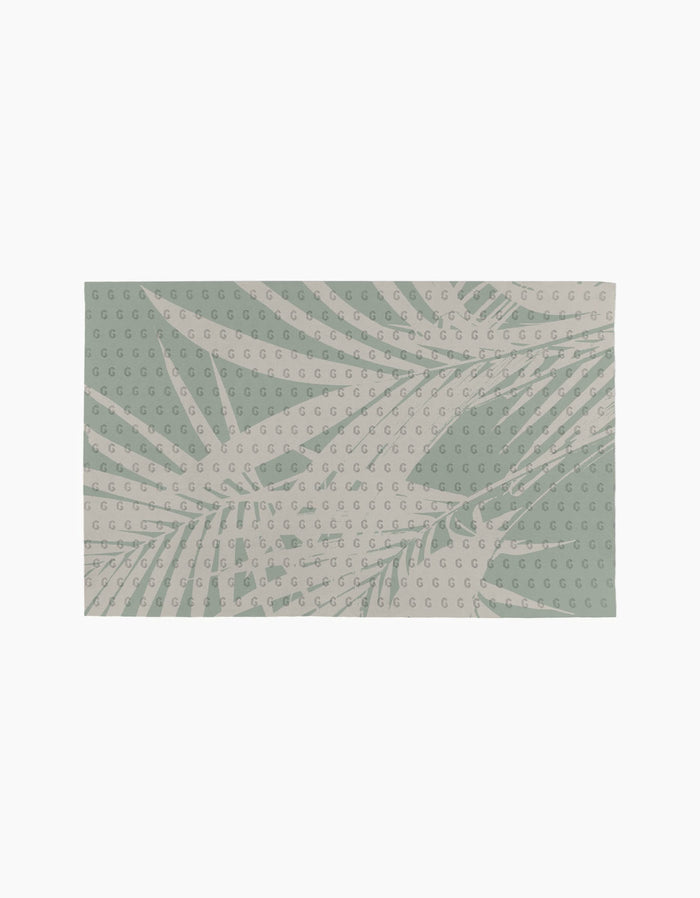 The Palm Breeze rug by Geometry features a light beige background with abstract green palm leaves and a repeating small G motif, crafted from recyclable materials for an eco-friendly choice.