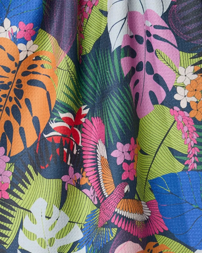 The GEOMETRY Palm Party kitchen towel features colorful recycled fabric with tropical leaves in orange, pink, blue, green, and white, plus a vibrant bird and small pink and orange flowers among the foliage.