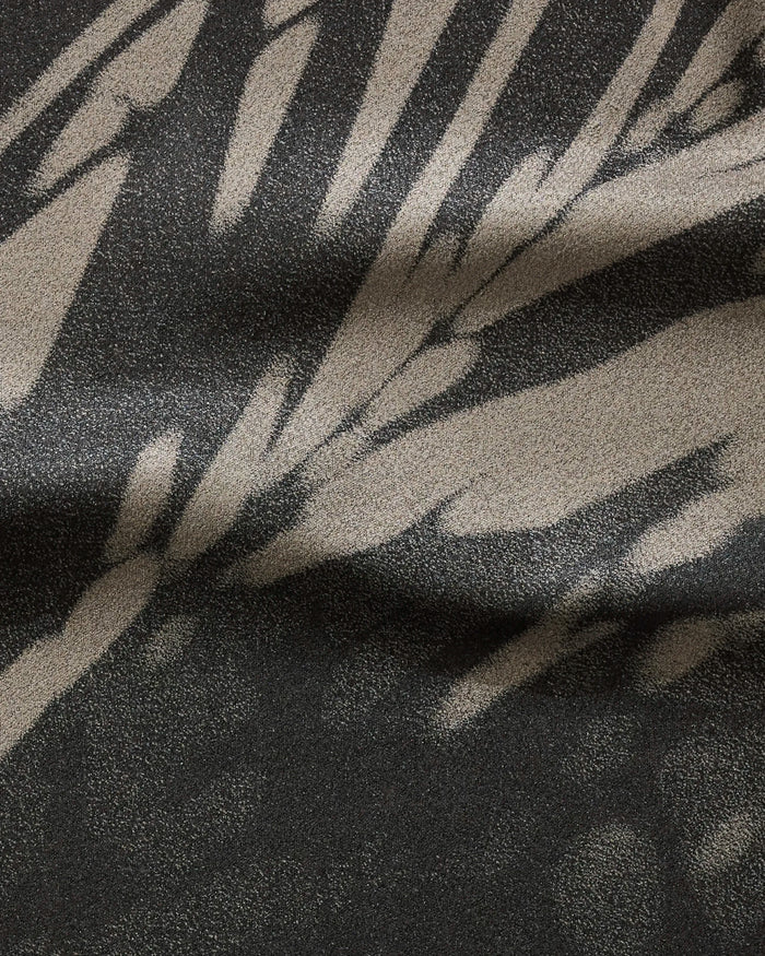 A close-up of GEOMETRY's Palm Shadow shows its ultra-absorbent, textured fabric made from recycled materials, featuring an abstract organic pattern in gray and beige that mimics soft shadows across the surface.