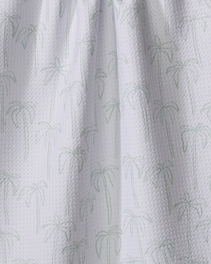 The Palms tea towel by Jen B. Peters features a white textured fabric with a subtle light green palm tree pattern. Made from quick-drying recycled materials, its gentle folds create soft shadows for a stylish, eco-friendly look.