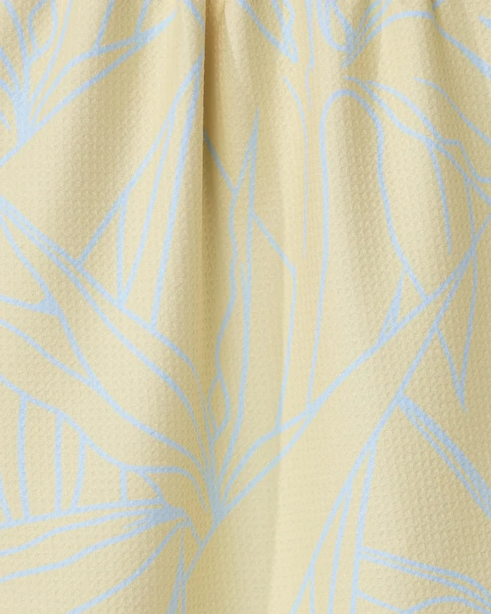 Close-up of the Paradise Blooms tea towel by GEOMETRY, featuring a textured light yellow fabric with a subtle blue abstract leaf pattern and soft folds near the top.