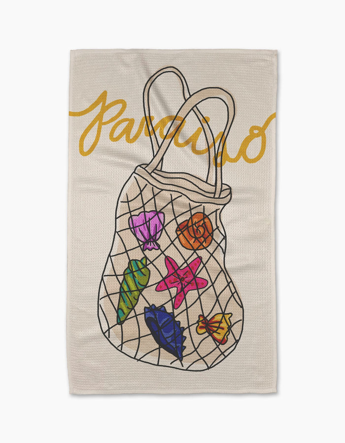 The Geometry Paraiso towel features ultra-absorbent Geoweave™ fabric, “Paraiso” in yellow cursive at the top, and a mesh bag illustration holding colorful seashells, a starfish, and seaweed.