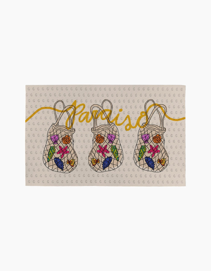 The Geometry Paraiso towel is rectangular and eco-friendly, showcasing three netted bags filled with colorful fruits. Paraiso appears in yellow script above the bags on a subtly patterned light background.
