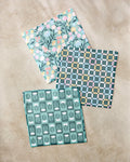 Three patterned Park Lane dishcloths by Charlie Rowan Designs, made from recycled materials, are laid on a beige surface: one with pink and yellow florals, one checkered, and one with white tulips on green.