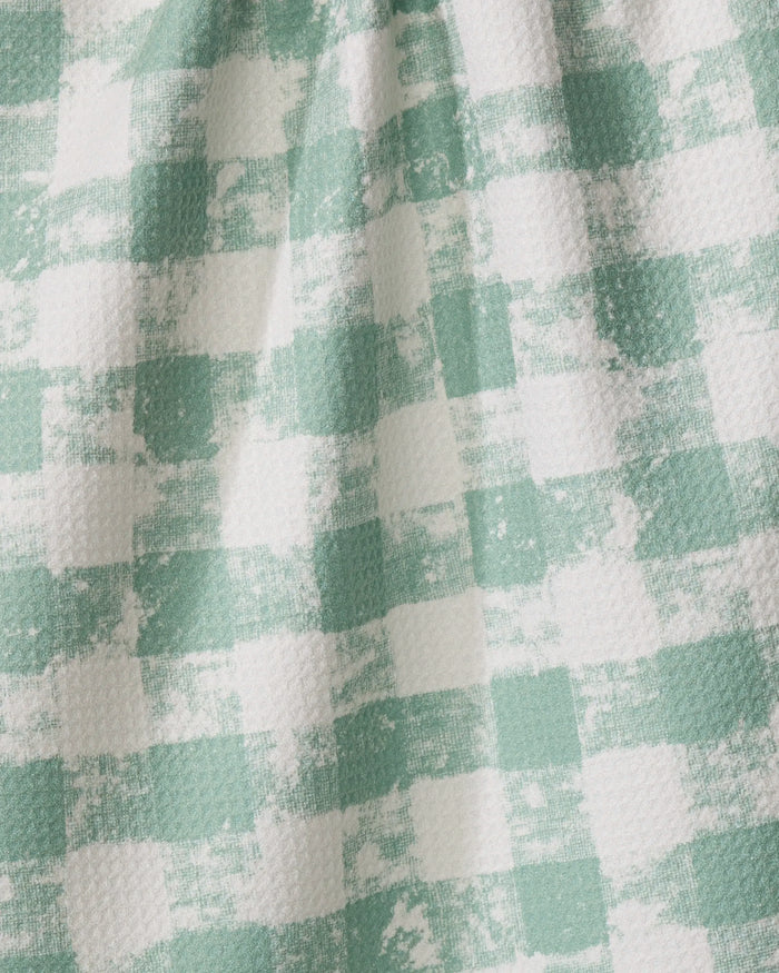 A close-up of the Geometry Patch Mint kitchen tea towel, crafted from recycled materials and featuring a green and white checkerboard pattern with a distressed look. Folds and shadows highlight its textured, ultra-absorbent surface.