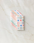 Six Patchwork Picnic kitchen towels by Brittany Jepsen, featuring a colorful geometric star pattern, are neatly folded and stacked on a light marble surface.