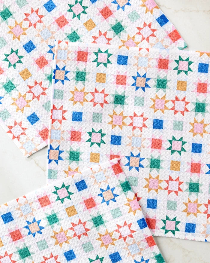 Four super-absorbent Patchwork Picnic dishtowels by Brittany Jepsen, featuring a colorful geometric star and square pattern in red, blue, green, and orange, made from recycled materials and displayed on a light surface.