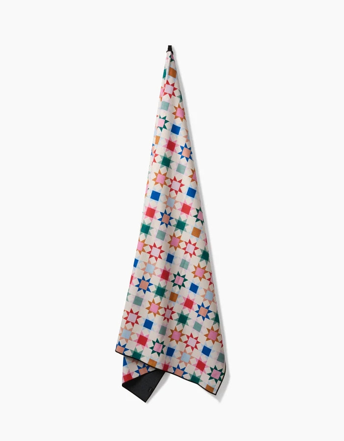 Patchwork Picnic by Brittany Jepsen is a quick-drying towel featuring a vibrant geometric star design in red, blue, green, orange, and pink on white, displayed against a white background.