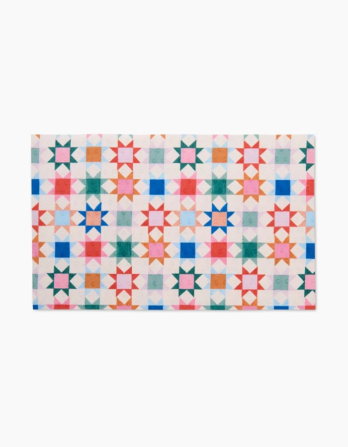 The Patchwork Picnic quilt by Brittany Jepsen features geometric stars in colorful grids on white, crafted from eco-friendly post-consumer recycled materials for sustainable style.