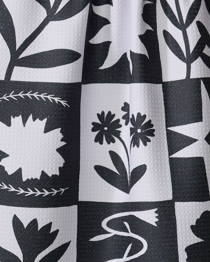 The "Patchwork" dish towel by Elana Gabrielle features a black and white grid pattern with stylized floral and leaf designs. Ultra-absorbent with visible texture, it’s both functional and beautifully crafted.