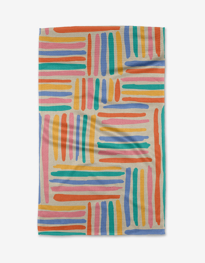 The Sareka Unique “Pathways” Geoweave™ tea towel features a colorful, abstract pattern of orange, blue, pink, teal, purple, and yellow brushstroke lines on a light background—crafted from recycled materials.