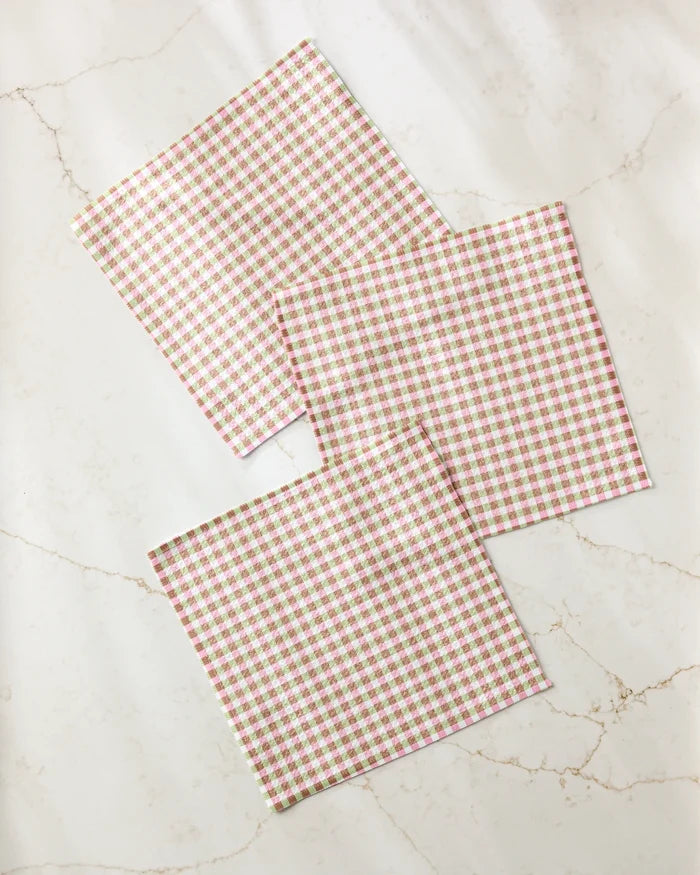 Three Patricia Plaid squares by Laura Prietto, featuring a pink and white gingham check and crafted from recycled materials, are slightly overlapped on a white marble surface.
