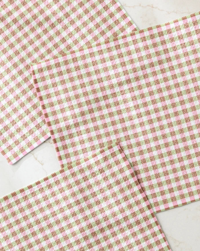 Three Patricia Plaid placemats by Laura Prietto, featuring a pink, brown, and white gingham pattern, are arranged on a marble surface. Made from recycled materials for an eco-friendly touch.