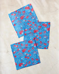 Three blue cloth napkins with red and white floral designs from Second Nature Studio’s Patriotic Garden set are arranged on a light marble-like surface.