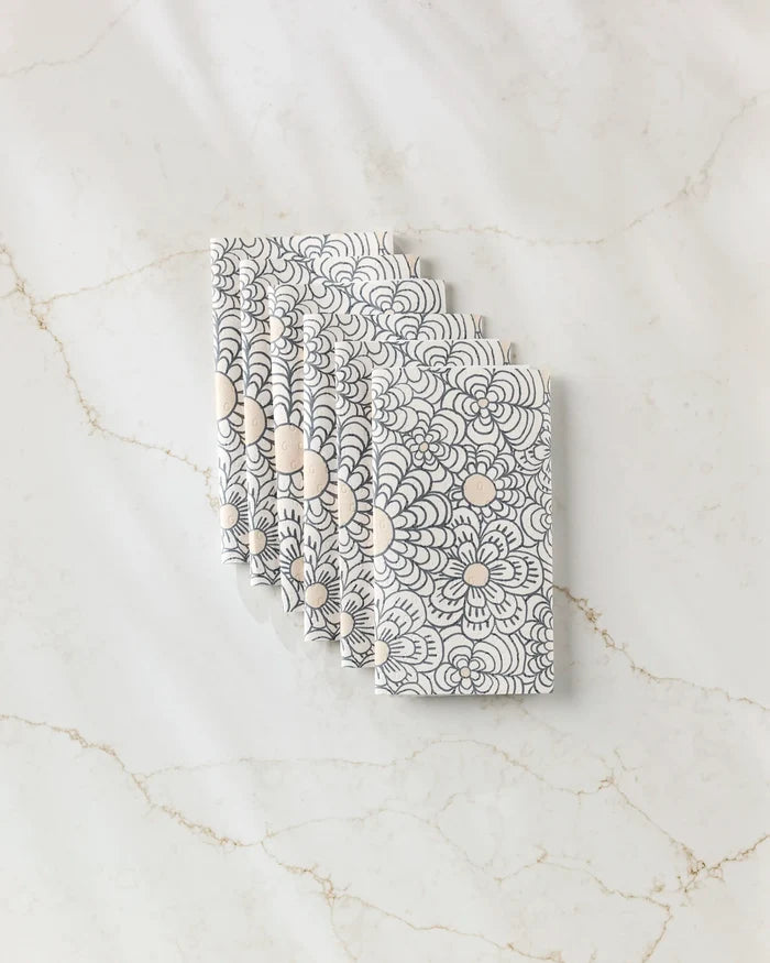 Six folded Paulette reusable paper towels by Amy MacCready, featuring a black and beige floral and circular pattern, arranged in a fanned-out stack on white marble with light brown veining.