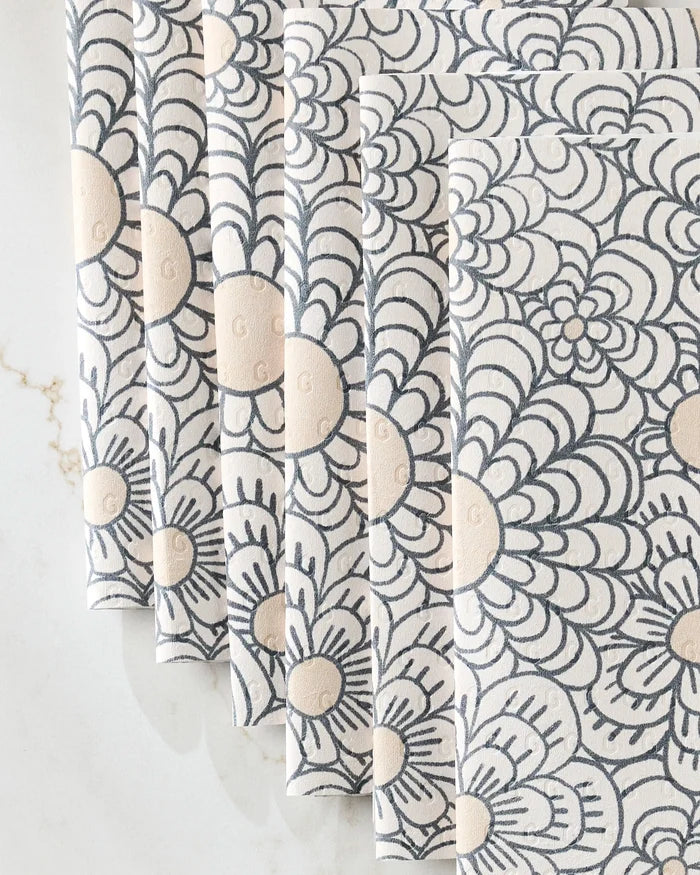 Paulette fabric napkins by Amy MacCready feature a repeating grey and beige floral pattern, elegantly fanned on marble—a chic, eco-friendly alternative to disposable or reusable paper towels.