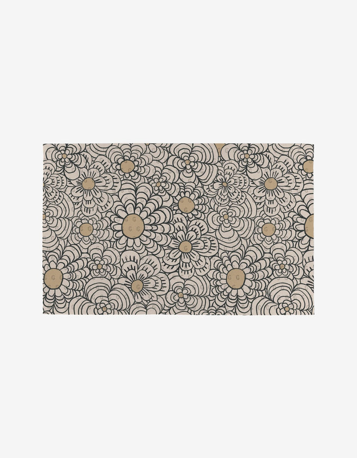 The Paulette mat by Amy MacCready features an intricate hand-drawn black floral pattern with gold circles on beige, crafted from eco-friendly post-consumer recycled materials.