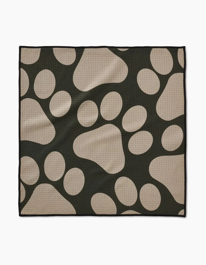 The Geometry Paw Prints mat is a black, rectangular towel with large tan paw prints on its ultra-absorbent, textured surface. Made from recycled materials, it has a clean black border for a simple finish.