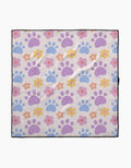The Paws and Daisies dog towel by Letters By Shells is highly absorbent, made from recycled materials, and features pastel blue and purple paw prints with pink, orange, and yellow flowers on a light background with a slim black border.
