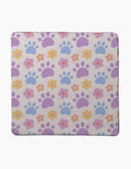 The Paws and Daisies dog towel by Letters By Shells showcases a pastel print of purple and blue paw prints with pink, yellow, and orange flowers on a light beige background.