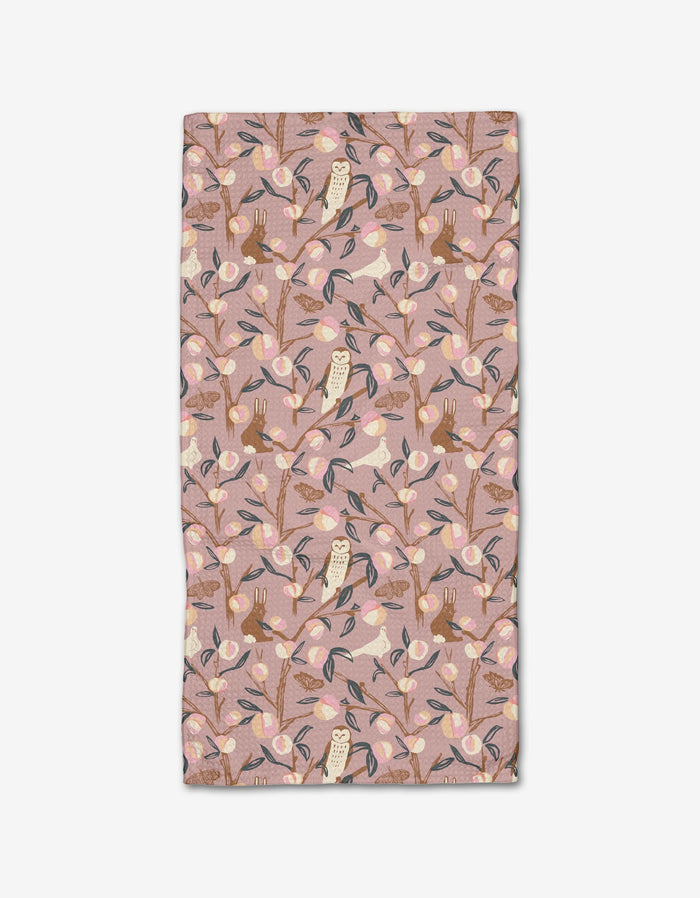 The Elisabeth Wing Peach Tree bar towel features a whimsical pattern of owls, rabbits, and birds among branches on a light pink background, crafted from recycled materials in soft pink, beige, brown, and blue tones.