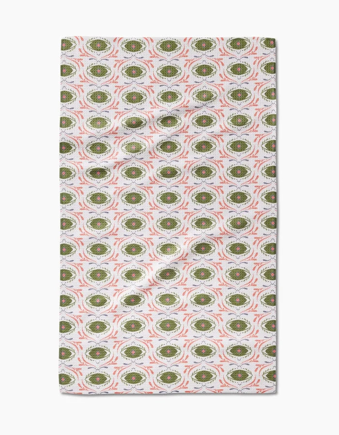 Peacock Eyes tea towel by Amita Nair features a repeating green and white oval pattern with red accents on a light background. This absorbent, quick-drying towel is slightly wrinkled and perfect for everyday kitchen use.