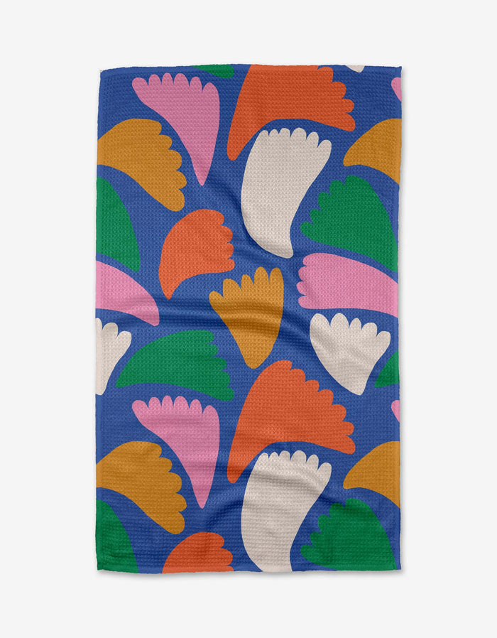 The Peacock Flowers tea towel by Jennifer Bouron is blue and rectangular, made from recycled materials, and features a random pattern of abstract fan-shaped forms in pink, orange, green, white, and peach.