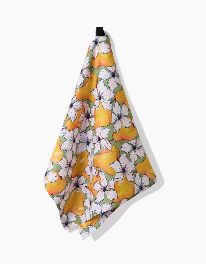 The Pears Petals tea towel by Maayan Alper-Swan, made from recycled materials, displays a vibrant design of yellow lemons and white flowers and hangs from a black hook against a white background.