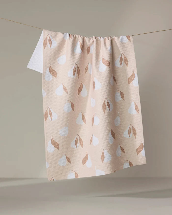 The "Pears" kitchen tea towel by Hufton Studio, in peach with white pears and brown leaves, made from recycled materials, hangs on a clothesline against a neutral background.