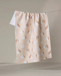 The "Pears" kitchen tea towel by Hufton Studio, in peach with white pears and brown leaves, made from recycled materials, hangs on a clothesline against a neutral background.