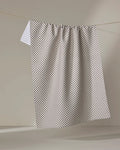 The Pebble kitchen tea towel by Jenny Keller features a pattern of small black dots on white and hangs from a clothesline against a light background. Made from recycled materials, it combines style with eco-friendly design.