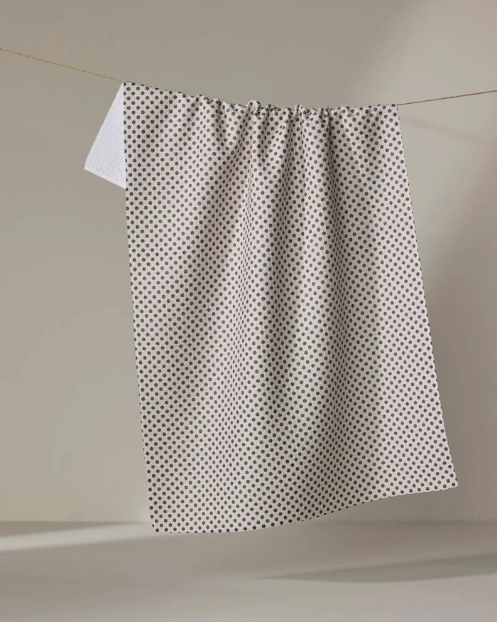 The Pebble kitchen tea towel by Jenny Keller features a pattern of small black dots on white and hangs from a clothesline against a light background. Made from recycled materials, it combines style with eco-friendly design.
