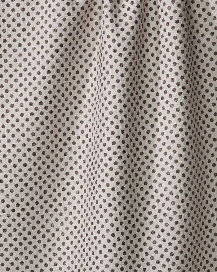 Close-up of the Pebble tea towel by Jenny Keller, crafted from beige fabric with evenly spaced small black polka dots. Soft vertical folds and shadows add texture and charm to this practical kitchen essential.