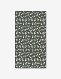 The Penelope napkin by Charlie Rowan Designs is a rectangular, dark green fabric napkin made from recycled materials and features a pattern of light beige leaves and branches.