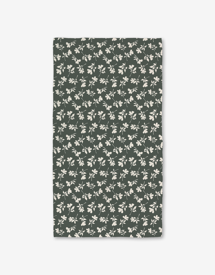The Penelope napkin by Charlie Rowan Designs is a rectangular, dark green fabric napkin made from recycled materials and features a pattern of light beige leaves and branches.
