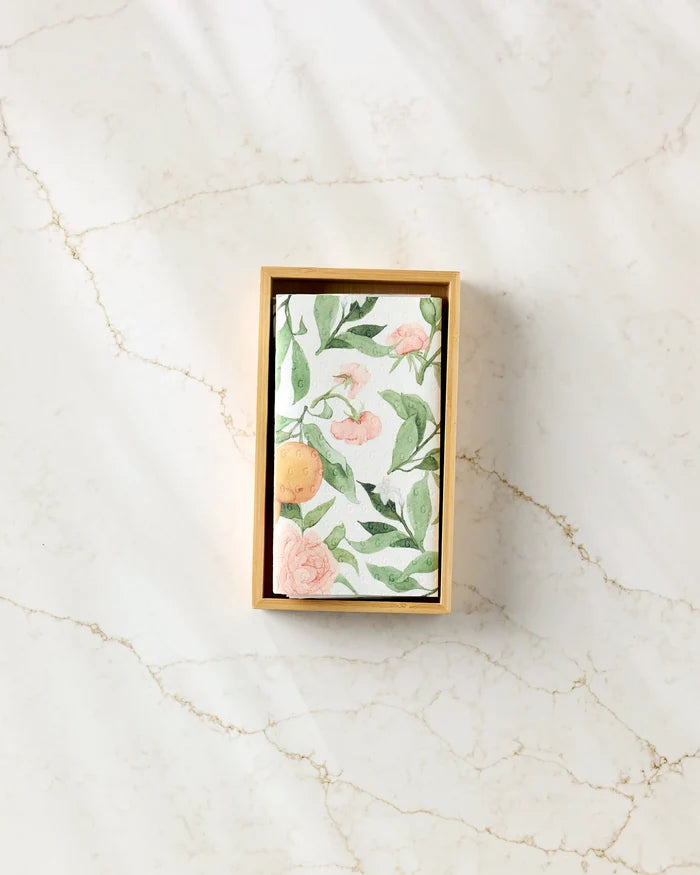Aubrey Fairchild’s “Peony For Your Thoughts” features a rectangular box with a floral and citrus card inside, set on veined marble—an elegant way to present eco-friendly kitchen towels.