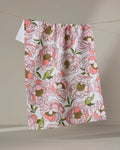 The Shelley Smith "Peony Paradise" kitchen towel, designed with eco-friendly materials and a pink and green large-bloom floral print, hangs on a string against a neutral background.