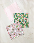 The Peony Paradise dishcloth set by Shelley Smith includes three stylish cloths—a light pink, an abstract green and pink, and a pink-and-white floral—crafted from recycled materials.
