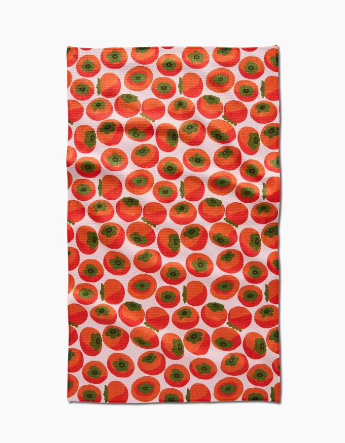 A rectangular kitchen tea towel by Katie OShea, called Persimmons, made from Geoweave fabric and featuring a vibrant, playful design of evenly spaced red and green persimmons on a white background.